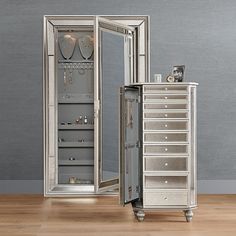 an open mirrored jewelry cabinet next to a silver dresser with its doors open on a wooden floor