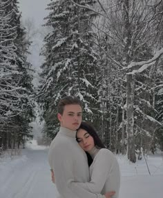 two people hugging each other in the snow near some trees and snow covered ground with lots of snow on it