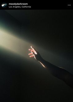 a person reaching out their hand towards the light coming through them on a dark background