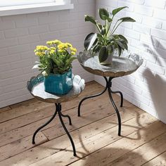 two small tables with plants on them in front of a white brick wall and wooden floor