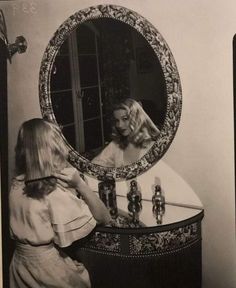 a woman standing in front of a mirror looking at herself in the mirror and brushing her hair