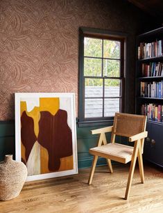 a room with a chair, bookshelf and a painting on the wall in it