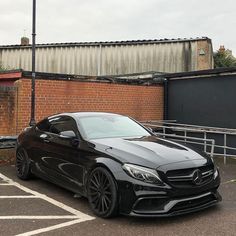 a black mercedes cla parked in a parking lot next to a brick wall and fence