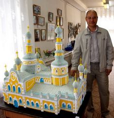 a man standing in front of a cake shaped like a building with yellow and blue domes