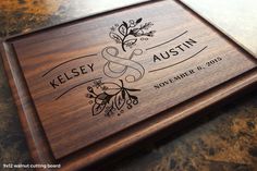 a wooden cutting board with the name and date engraved on it, sitting on a table