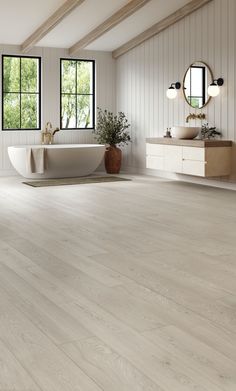 a large white bathroom with wood flooring and tub in the center, windows on both sides