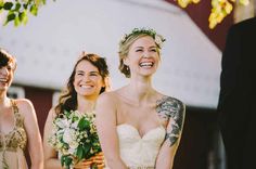 two women smile as they stand next to each other with flowers in their hair and tattoos on their arms