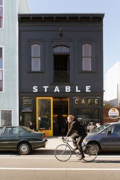 a man riding a bike down a street next to parked cars and tall black buildings