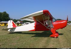 a small red and white plane parked on top of a grass covered field