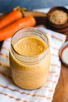 a glass jar filled with liquid sitting on top of a table next to carrots