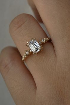 a woman's hand with a diamond ring on top of her finger and an emerald stone in the middle