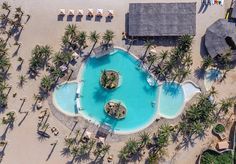 an aerial view of a resort pool and beach with palm trees in the foreground