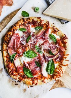 a pizza sitting on top of a wooden cutting board next to cheese and basil leaves