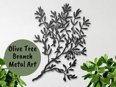 an olive tree branch metal art hanging on the wall next to some potted plants