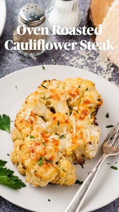 a white plate topped with cauliflower steak covered in cheese and parsley next to a fork