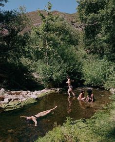 three people are playing in the water near some rocks and trees, while one person is swimming