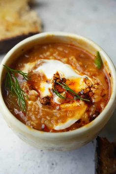 a close up of a bowl of soup on a table with bread in the background