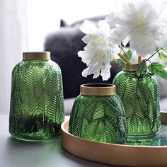 three green glass vases sitting on top of a table next to a white flower