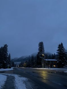 an empty street with snow on the ground and mountains in the background at night time