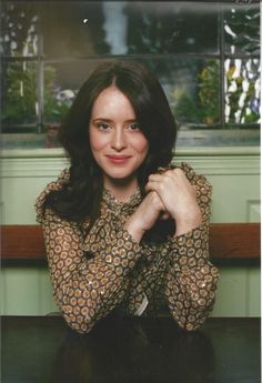 a woman sitting at a table with her hands on her chest and looking into the camera