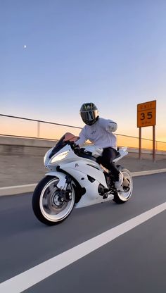 a man riding on the back of a white motorcycle down a highway next to a speed limit sign