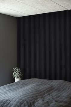 a bedroom with black vertical blinds on the wall and a plant in the corner next to the bed