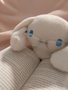 a white stuffed animal with glasses on it's head is reading a book in bed