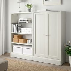 a white bookcase with two doors and drawers in a living room next to a potted plant