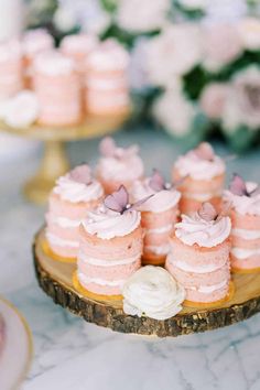 small pink cakes and cupcakes on a wooden platter with flowers in the background