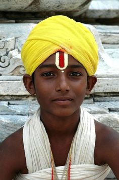 a young boy wearing a yellow turban and red beads on his head is looking at the camera