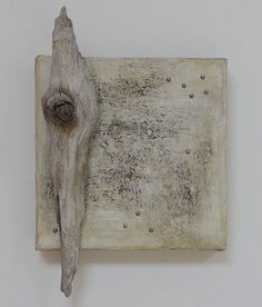 a piece of driftwood on a white wall with holes in the middle and a wooden stick sticking out of it