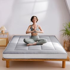 a woman is sitting in the middle of a yoga pose on a mattress with her hands together