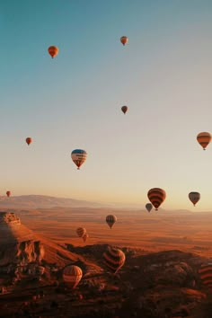 many hot air balloons are flying in the sky above some mountains and deserts at sunset