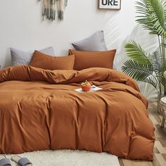 a bed with an orange comforter on top of it in a bedroom next to a potted plant