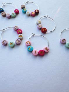 three pairs of hoop earrings with letters on them sitting on a white surface, one is pink and the other is blue