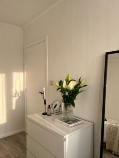 a vase with flowers sitting on top of a white dresser next to a large mirror