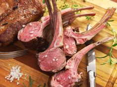 some meat is sitting on a cutting board next to a knife and fork with herbs