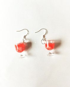 a pair of red wine glasses hanging from silver earwires on a white surface