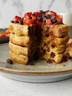 a stack of waffles with chocolate chips and strawberries on top sitting on a plate