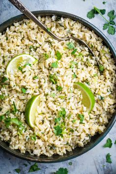 a bowl filled with rice, limes and cilantro next to a spoon