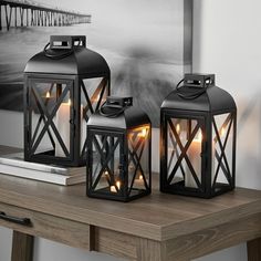 three black lanterns sitting on top of a wooden table