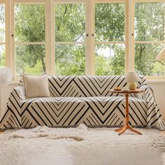 a living room filled with furniture next to two large windows and a rug on the floor