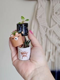 a hand holding a small plant in a pot with tiny animals on the top and plants growing out of it