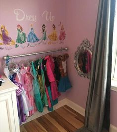 there are many princess dresses hanging on the rack in this girls's room with pink walls and hardwood floors