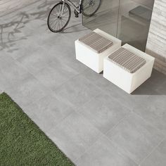 a bike parked next to a white bench on top of a cement floor in front of a building