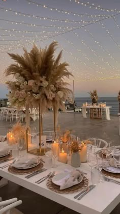 a table set up with place settings and candles for an outdoor dinner by the ocean