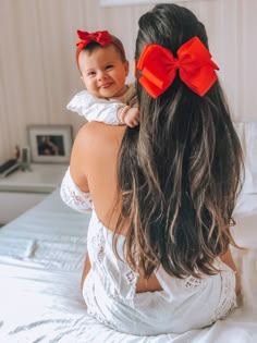 a woman holding a baby in her arms on top of a bed with white sheets