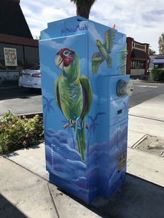 a blue box with a painting of a parrot on it's side next to a tree