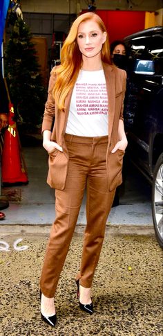 a woman standing in front of a car wearing brown pants and a t - shirt