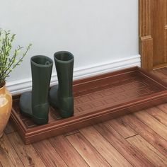 two green rubber boots sitting on top of a wooden floor next to a planter